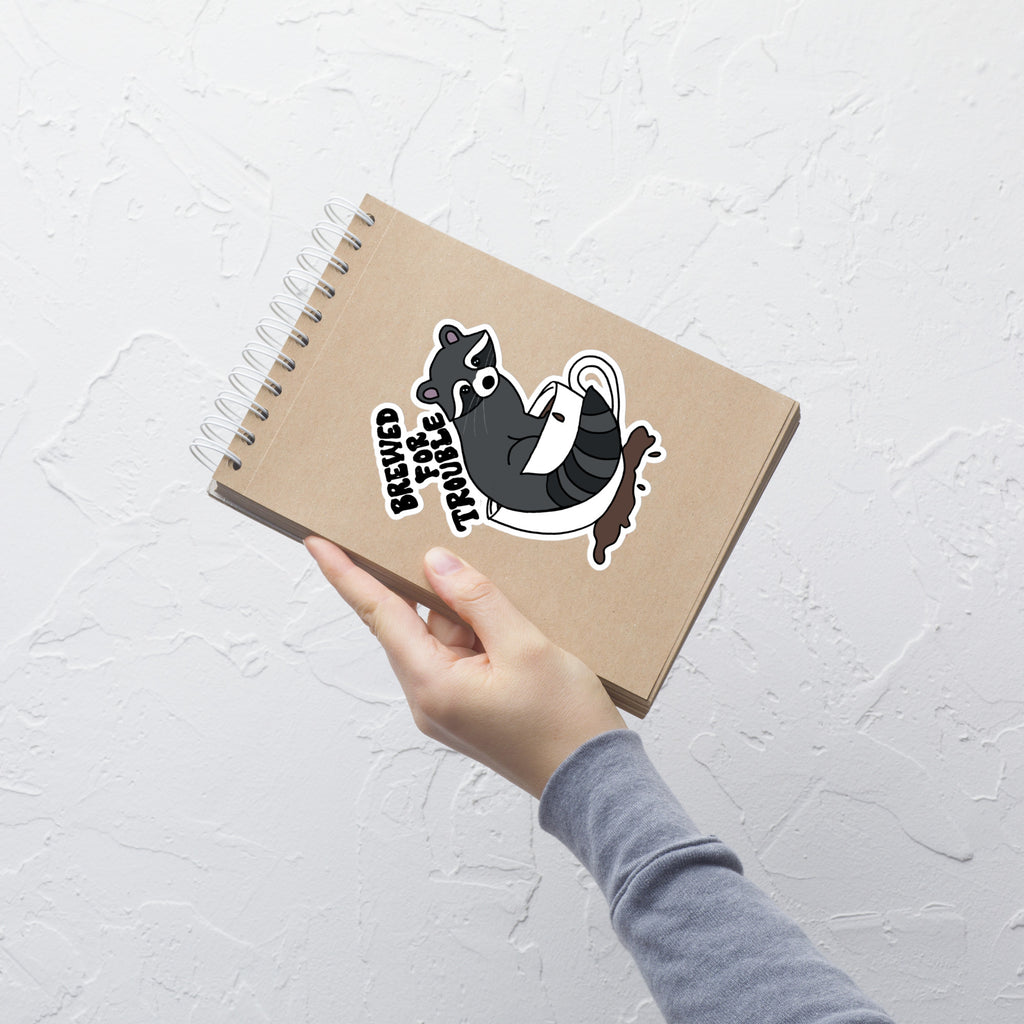 Raccoon Brewed for Trouble die-cut satin sticker by Petals & Ash Studio, featuring a playful raccoon design on a 6x6 inch sheet.